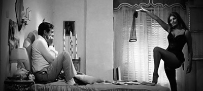 A black and white photo of Sophia Loren and Marcello Mastroianni in a bedroom while Sophia is doing one of the most famous streptease scene of the cinema. The scene is from the third episode of Yesterday, Today and Tomorrow